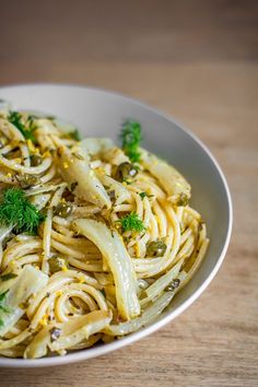 a white bowl filled with pasta and parsley on top of a wooden table next to a fork