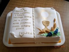 a cake decorated with an open book and a chalice on the front, sitting on top of a wooden table