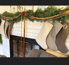 stockings hanging from a mantel over a fireplace with evergreen garland on it and candles