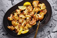 roasted cauliflower with lemon wedges on a black plate