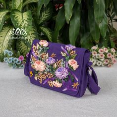 a purple bag with flowers on it sitting in front of some potted plants and greenery