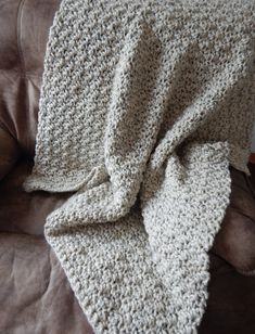 a crocheted blanket sitting on top of a brown couch next to a pillow