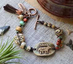 a bracelet with beads and charms on top of a wooden table next to a potted plant