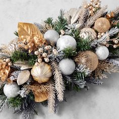 an arrangement of christmas ornaments and greenery on a marble surface with gold, silver and white decorations