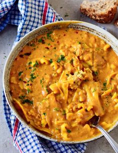 a bowl filled with pasta and cheese on top of a blue checkered cloth next to bread