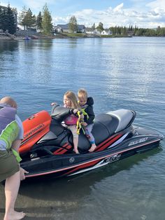 two children are sitting on the back of a jet ski while an adult looks on