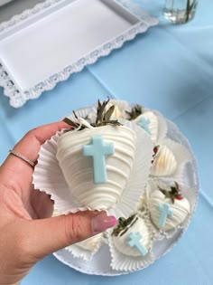 a hand holding a white chocolate covered in frosting with a cross on the top