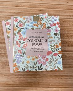 the crafting side coloring book is on a wooden surface with flowers and leaves around it