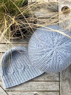 two knitted hats sitting on top of a wooden table next to grass and plants