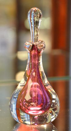 a pink glass bottle sitting on top of a table next to a mirror surface with reflections