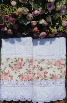 two white towels sitting next to each other on top of a wooden table covered in flowers