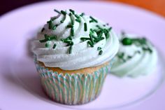 two cupcakes with white frosting and sprinkles on a plate