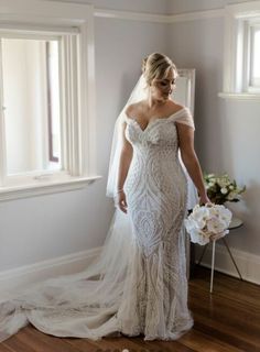 a woman in a wedding dress standing next to a window