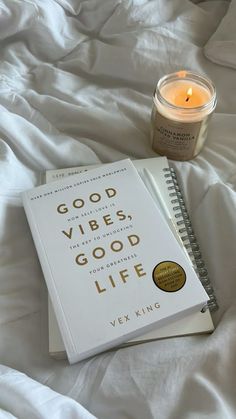 a book sitting on top of a white bed next to a candle and a cup