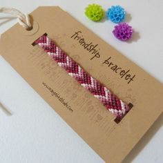 two small braided bracelets on a brown card with some colorful flowers in the background