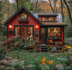 a small red house with lots of flowers in the front yard and windows on each side