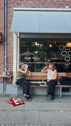 two women sitting on a bench in front of a store