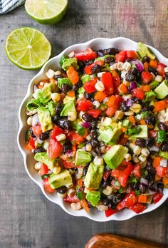 a white bowl filled with black beans, avocado and corn salad next to lime wedges