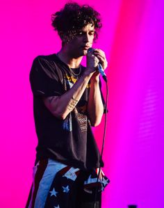 a man standing on top of a stage with a microphone in his hand and an american flag t - shirt