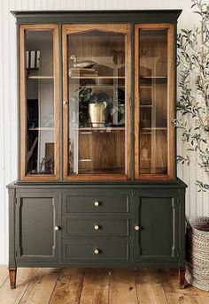 a green china cabinet with glass doors and drawers on the top, next to a potted plant