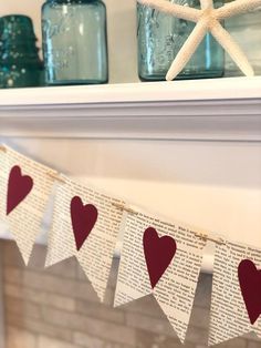 some red hearts are hanging from a mantle with books and mason jars in the background