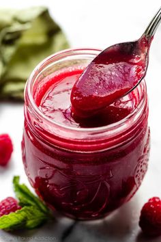 a spoon full of raspberry jam with fresh raspberries on the side