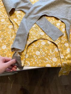 someone is cutting fabric on top of a yellow and white flowered cloth with scissors