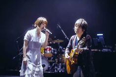 two people on stage with one holding a guitar and the other singing