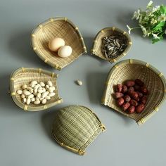 four baskets filled with nuts and vegetables on top of a gray surface next to a plant