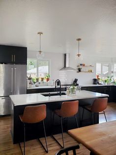 a kitchen with black cabinets and white counter tops, an island in the middle has four brown chairs