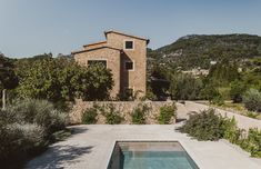 an outdoor swimming pool in front of a stone building with trees and bushes around it