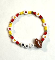 #87 football and hearts bracelet is your go to accessory for the big game! Mixed with red and yellow hearts and matching seed beads to show off your team spirit. Gold colored spacer ball beads are finished off with a football charm.  Bracelets are available in a variety of lengths.  Pick your custom length from the drop down menu below.  Please be aware that beading may slightly differ from what is pictured as to accommodate selected sizing.  All our bracelets are made with quality in mind.  With that being said, all bracelets should be treated with care while putting on, wearing, and taking off.  Keep dry. Do not swim or bath with them. Football Friendship Bracelet, Multicolor Team Spirit Beaded Bracelets For Game Day, White Beaded Bracelets For Football Season, Multicolor Beaded Bracelets For Game Day, Red Beaded Bracelets With Letter Beads For Game Day, Super Bowl Fashion, Friendship Jewelry, Yellow Heart, Heart Bracelet