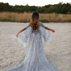 a woman standing in the sand with her arms spread out and wearing a white dress