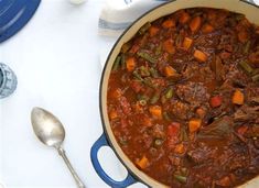 a large pot filled with stew next to a spoon and fork on a white table