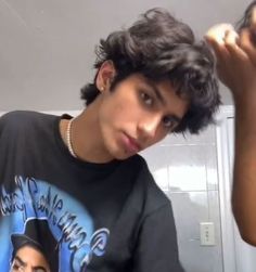 a young man brushing his hair in front of a mirror and looking at the camera