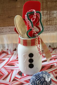 a snowman mason jar filled with kitchen utensils and candy canes on a table