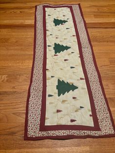 a quilted table runner with christmas trees on the bottom and red trimmings