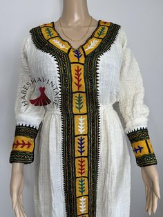 This stunning Habesha Kemis is crafted from 100% cotton Axum Shukor Menen fabric and adorned with 100% handmade Tibeb, reflecting the skill of Ethiopian artisans. Designed as one-size-fits-all, this dress offers comfort and style for any occasion. For custom sizing, send us your measurements, and we'll be delighted to create a personalized fit. Perfect for cultural celebrations, weddings, and more, this timeless piece is a celebration of Ethiopian heritage! Folk Style Cotton Dress With Traditional Patterns, Traditional Fitted Cotton Kaftan, Fitted Cotton Traditional Kaftan, Traditional Cotton Kaftan With Woven Motifs, Cotton Dresses With Traditional Embroidered Patterns, Cotton Dresses With Multicolor Embroidery And Traditional Patterns, White Fitted Cotton Kaftan, Traditional Patterned Cotton Kaftan For Festivals, Cotton Kaftan With Traditional Patterns For Festivals