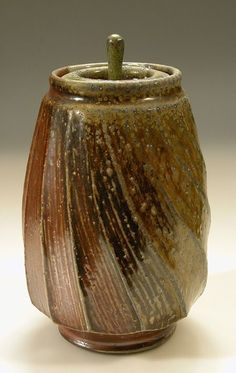 a brown and black ceramic container on a white surface with a small green object in the middle