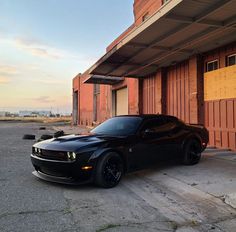 a black sports car parked in front of a building with an open garage door on the side