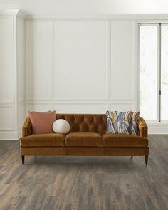 a brown couch sitting on top of a wooden floor next to a white wall and window