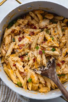 a white bowl filled with pasta and bacon on top of a table next to a wooden spoon