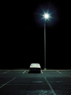 an empty parking lot with a car parked under a street light at night, in the dark