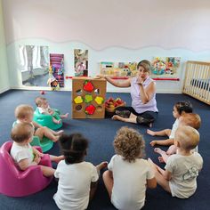 a woman sitting on the floor in front of a group of children playing with toys