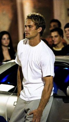 a man standing next to a silver car in front of a group of young people