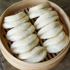 some white bread is in a bamboo basket on a wooden table with chopsticks