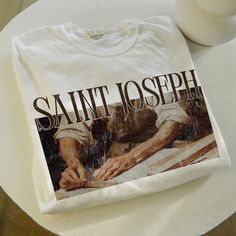 This "Saint Joseph" vintage graphic tee blends faith and style, featuring a classic design perfect for any Catholic wardrobe. Whether for baptisms, first holy communion, or as a confirmation gift, this shirt honors Saint Joseph, the father of Jesus. It's also an ideal gift for godfathers or anyone devoted to their faith. With its timeless, vintage aesthetic, this tee makes a unique and thoughtful addition to any believer's wardrobe. Show your love for Saint Joseph in a way that's both fashionabl Catholic St Joesph Tshirts, Vintage Christian Tshirt, Catholic Fashion, Catholic Shirt, Catholic Tshirts, Saints Shirts, Aesthetic Tshirt, Spiritual Clothing, Faith Based Clothing