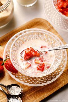 a bowl of yogurt with strawberries in it and two spoons on the side