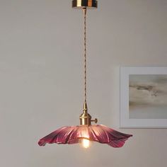 a pink flower hanging from a brass colored light fixture in a white room with a painting on the wall