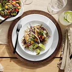 two plates with food on them sitting on a table next to glasses and utensils